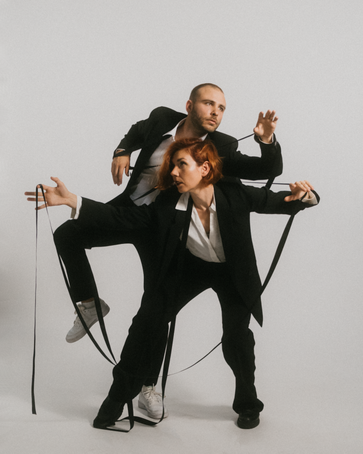 Frau und Mann posieren im schwarzen Anzug vor einem weißen Hintergrund