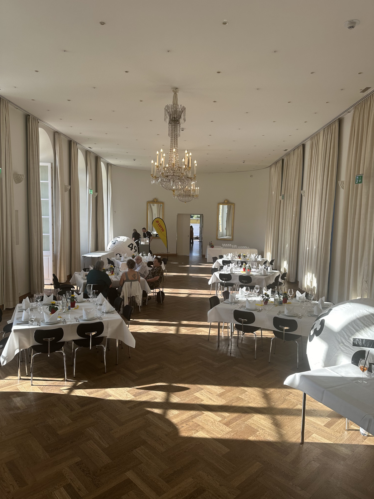 Saal mit Kronleuchter, großer Lottokugel und festlich gedeckten Tischen