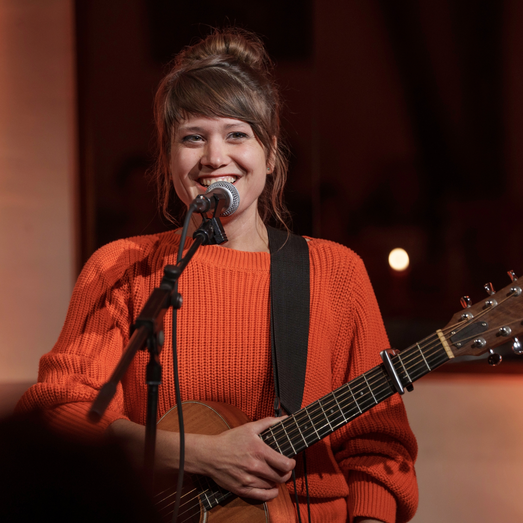 Elena Seeger mit Gitarre vor Mikro lächelt in die Kamera.