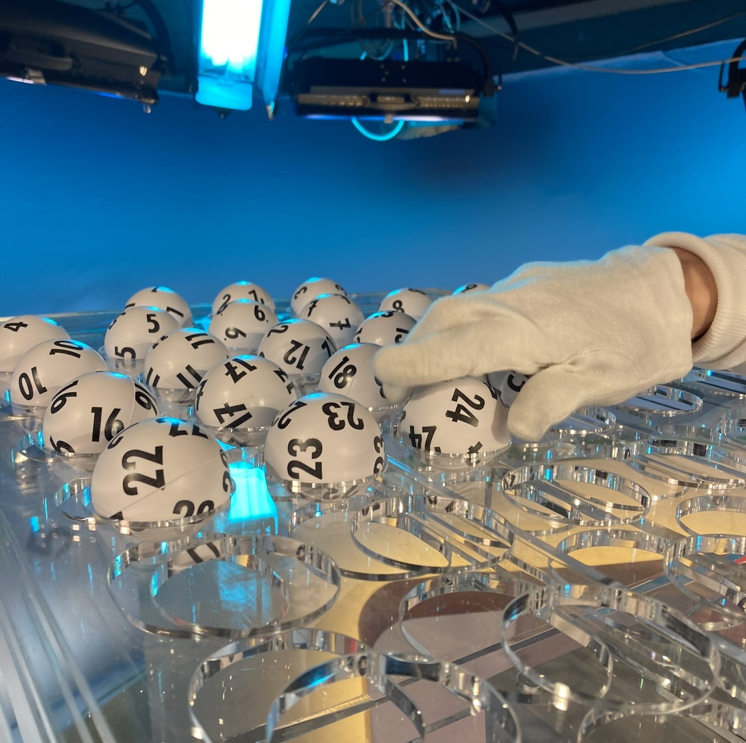 Hand platziert Lotteriekugeln auf einem Tablett im beleuchteten Lotto-Studio.