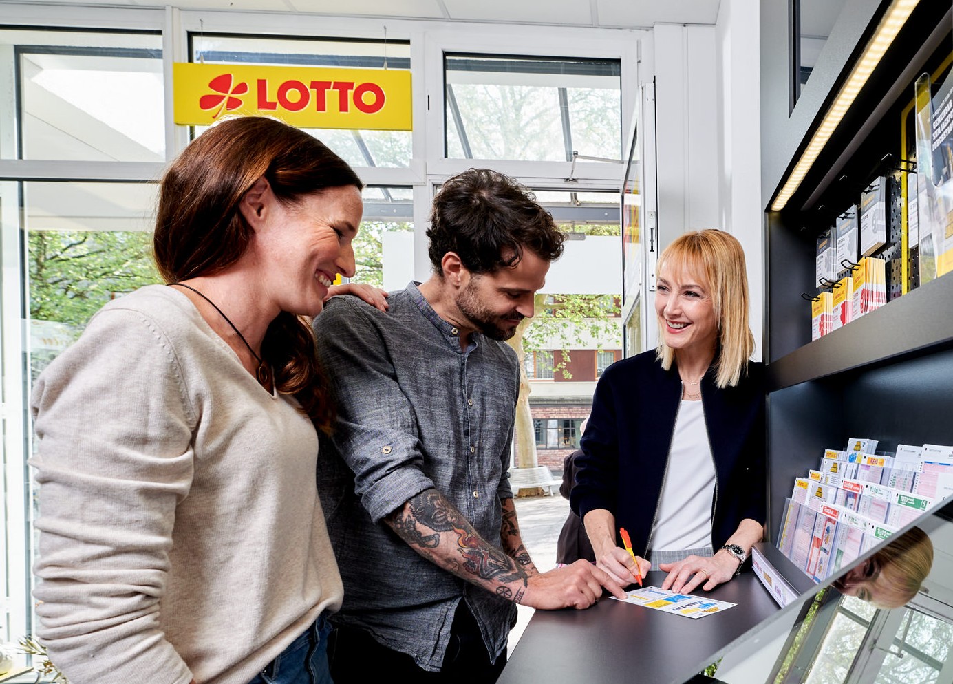 Drei Personen beim Lotto-Ausfüllen in Annahmestelle mit Beratung.
