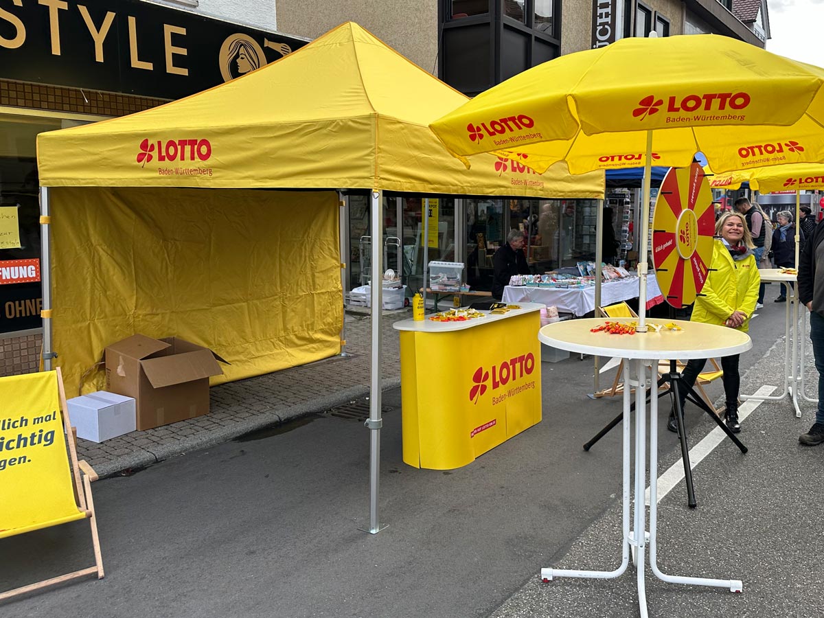 Aufgebauter Lotto-Pavillon mit Theke und Stehtisch vor einem Geschäft auf der Straße