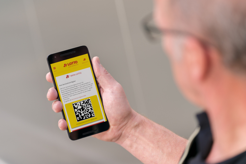 Mann hält Smartphone in der rechten Hand. Darauf zu sehen der QR-Code der ServiceCard digital.